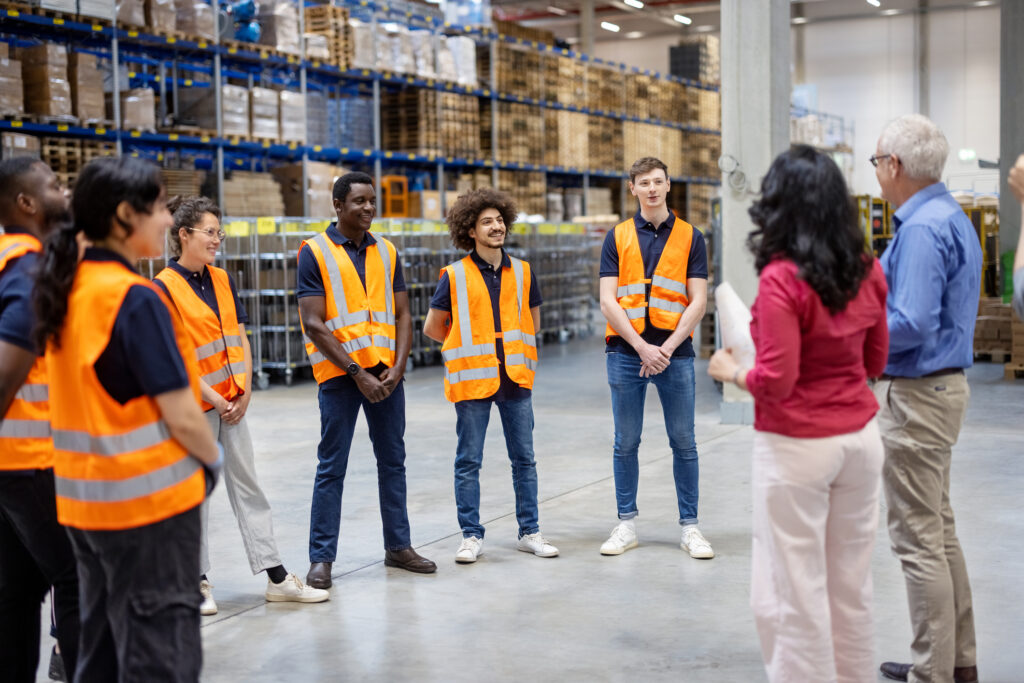 businessman and businesswoman meeting with warehouse employees. Group of employees discussing with manager during a meeting in warehouse.